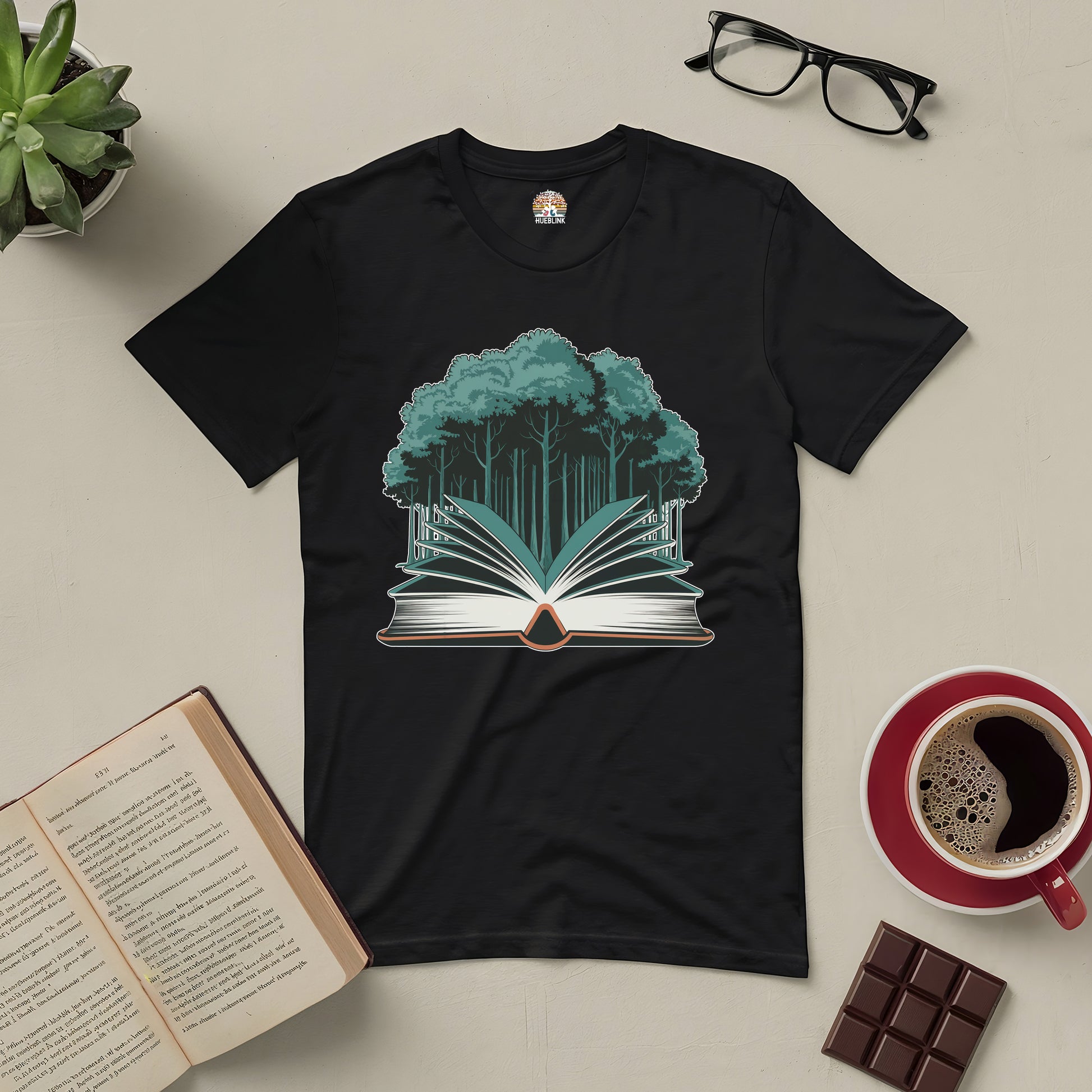 Black "Rooted in Story" tee featuring a forest growing from an open book, surrounded by coffee, chocolate, glasses, and an open book.