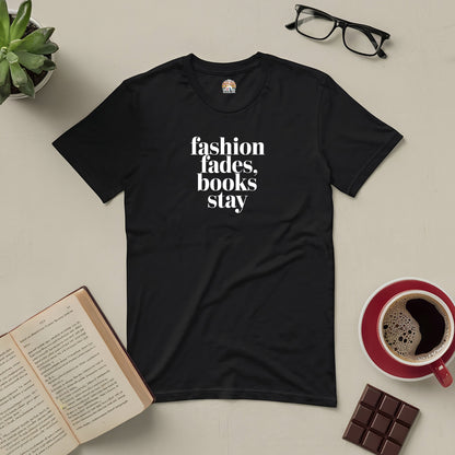 Black tee with "Fashion fades, books stay" text, surrounded by an open book, glasses, coffee, and chocolate bar.