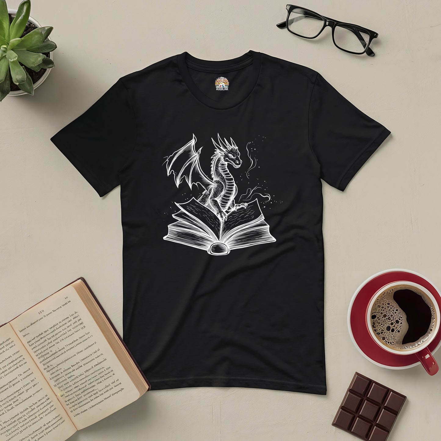 "Literary Dragon Tee featuring a mythical dragon emerging from a book, perfect for fantasy lovers. T-shirt displayed with coffee and books."