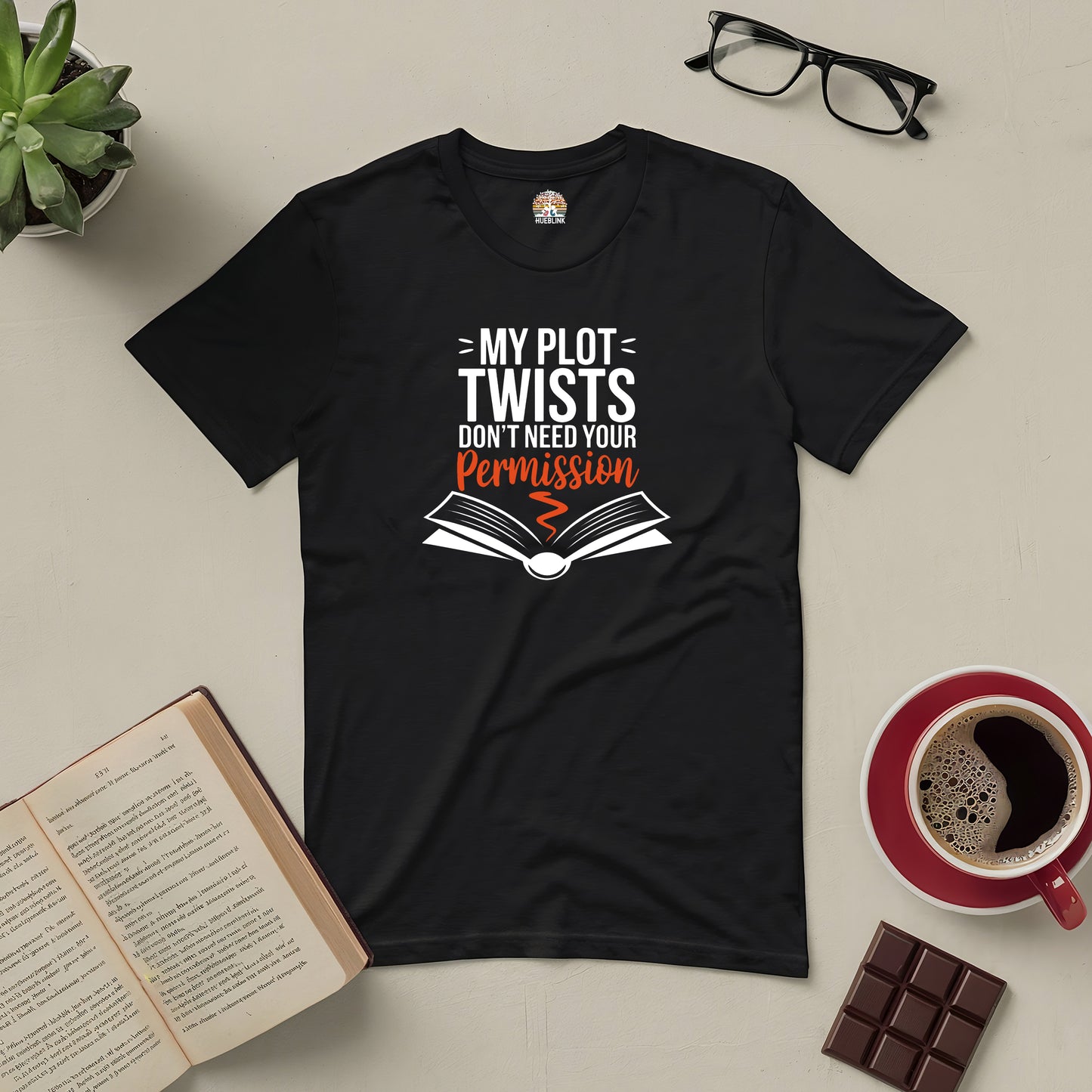 Black tee with "My Plot Twists Don't Need Your Permission" design, surrounded by glasses, book, coffee, and chocolate.