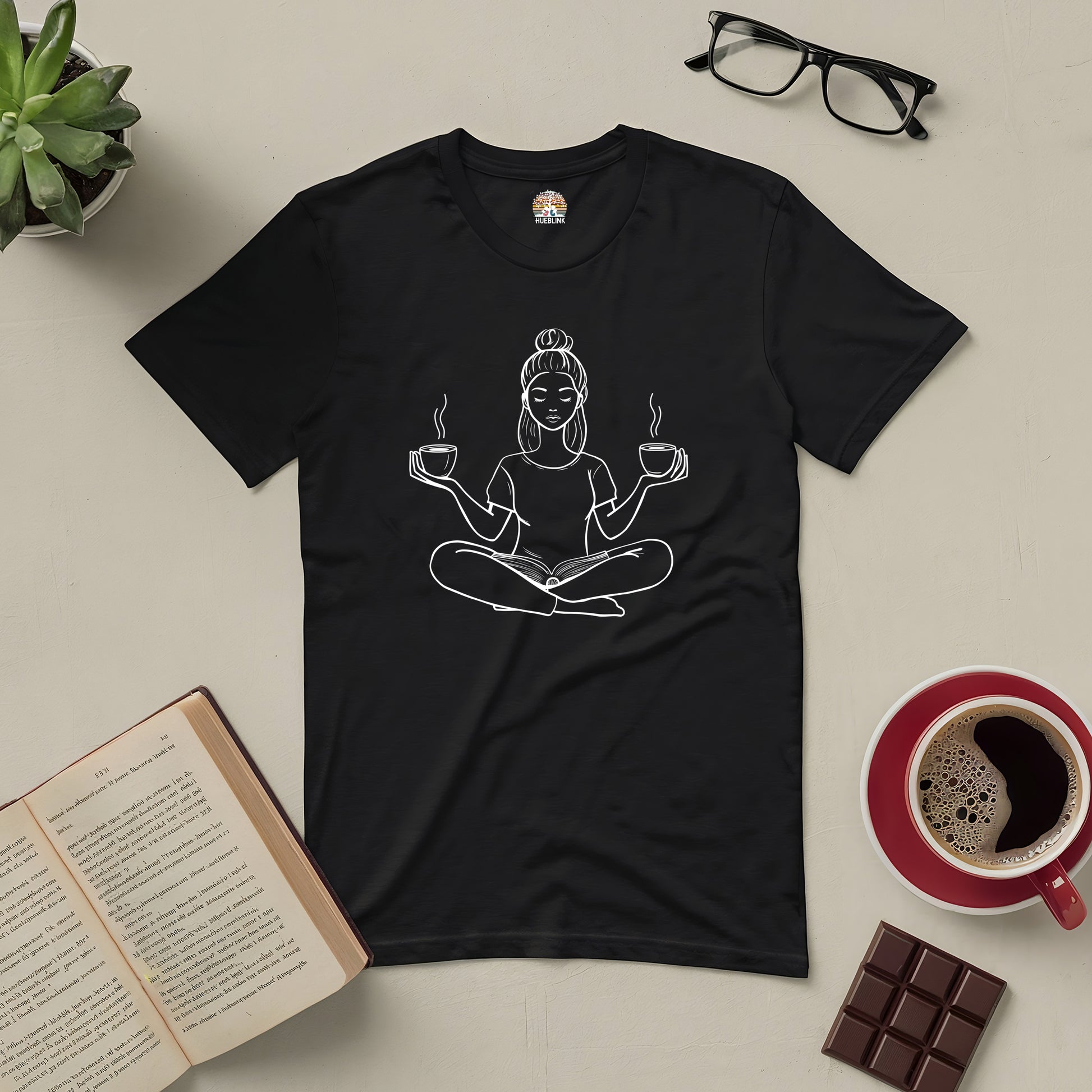 Black tee featuring design of a meditating figure with books and coffee, surrounded by an open book, eyeglasses, and a coffee cup.