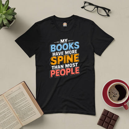 Black tee with "My Books Have More Spine Than Most People" text, surrounded by a book, coffee, chocolate, glasses, and a plant.