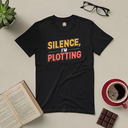 Black t-shirt with "Silence, I'm Plotting" design for book lovers and writers, surrounded by coffee, chocolate, and books.