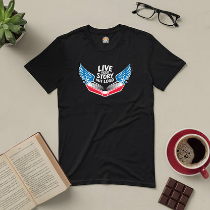 Black tee with open book and wings design, "Live Your Story Out Loud," on a table with glasses, coffee, chocolate, and a book.