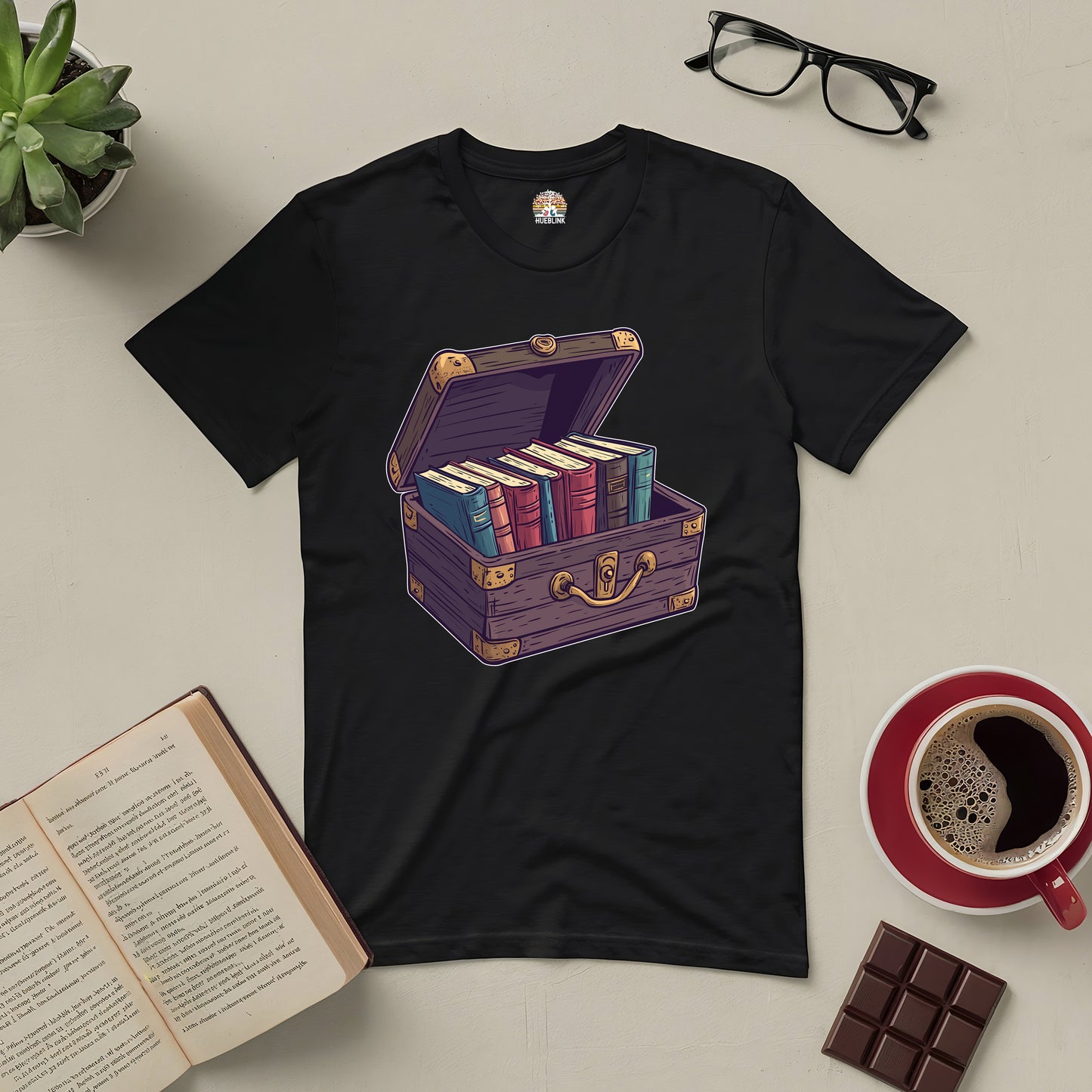 Black tee featuring a treasure chest filled with colorful books, perfect for book lovers. Surrounded by glasses, coffee, and an open book.