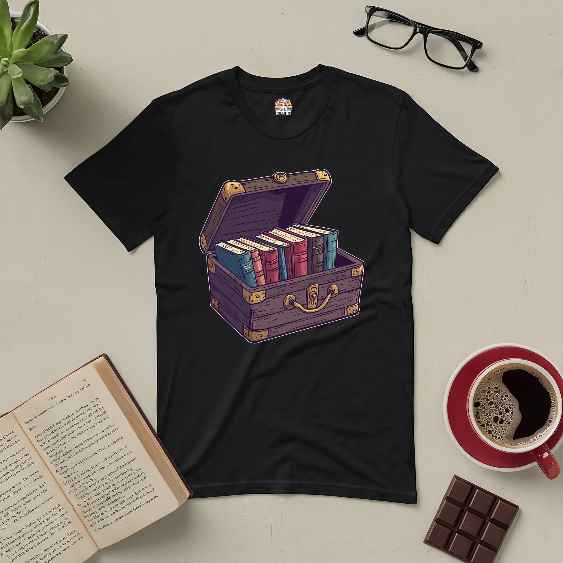 Black tee featuring a treasure chest filled with colorful books, perfect for book lovers. Surrounded by glasses, coffee, and an open book.