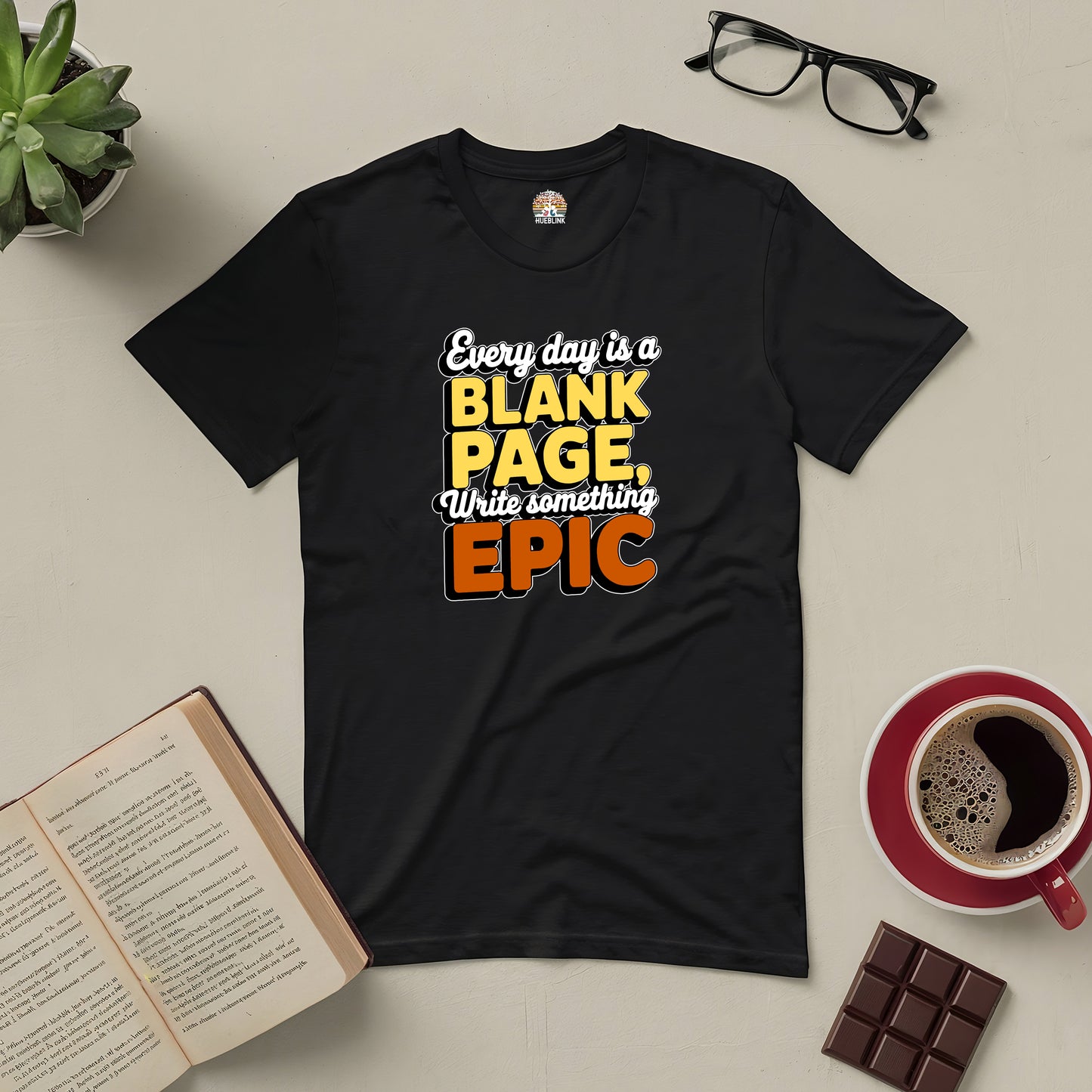 Black T-shirt with "Every Day is a Blank Page, Write Something Epic" message surrounded by book, coffee, glasses, plant, and chocolate.