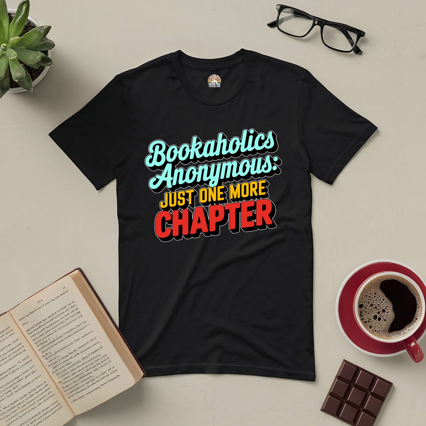 Bookaholics Anonymous Tee with the slogan "Just One More Chapter" surrounded by books, coffee, and chocolate.