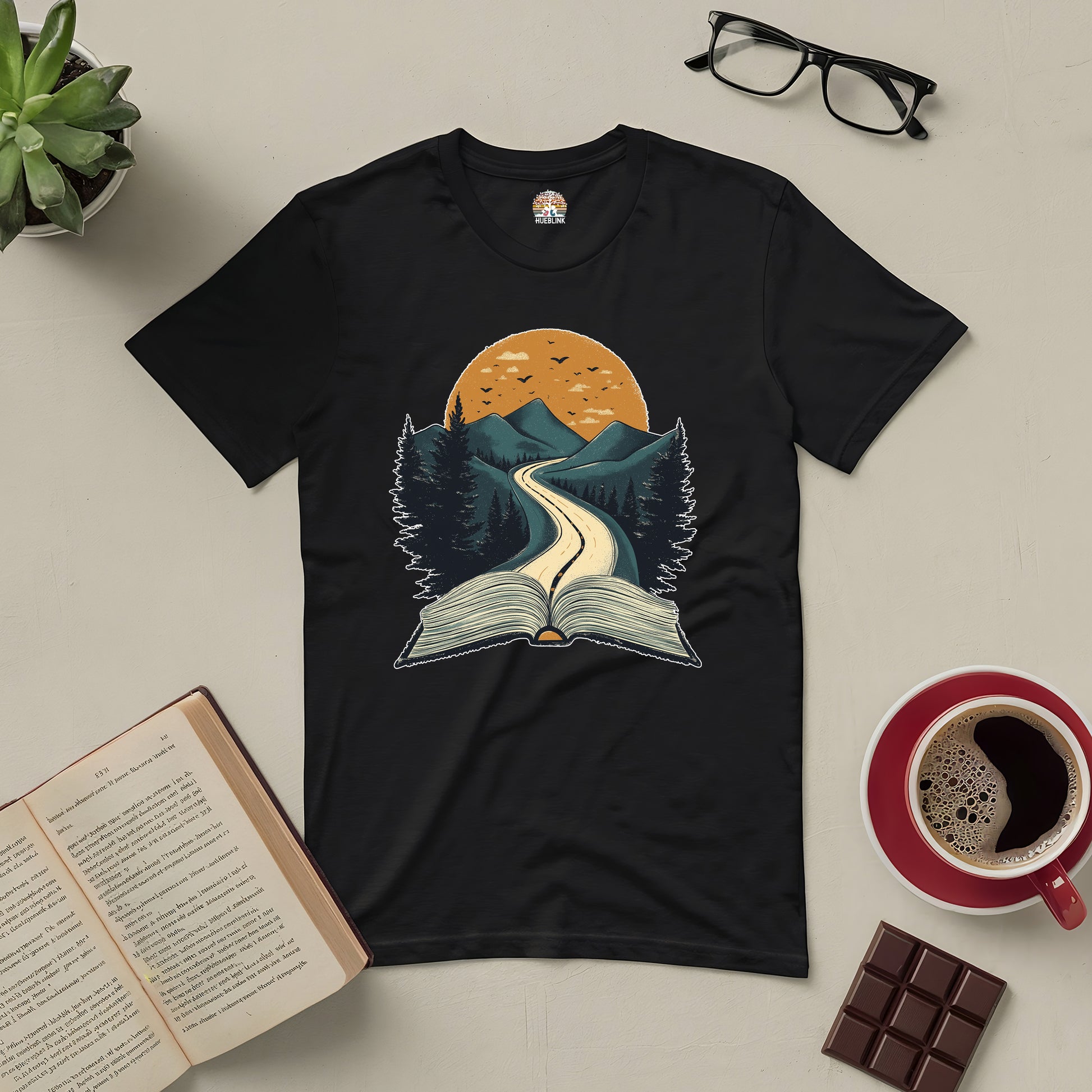 Starting Point Tee with a road emerging from an open book under a sunset, surrounded by nature, perfect for readers and adventurers.