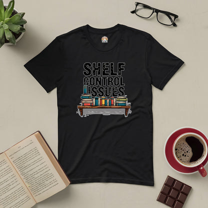 Witty "Shelf Control Issues" tee for book lovers, featuring a stack of books on a black t-shirt, surrounded by coffee and reading essentials.