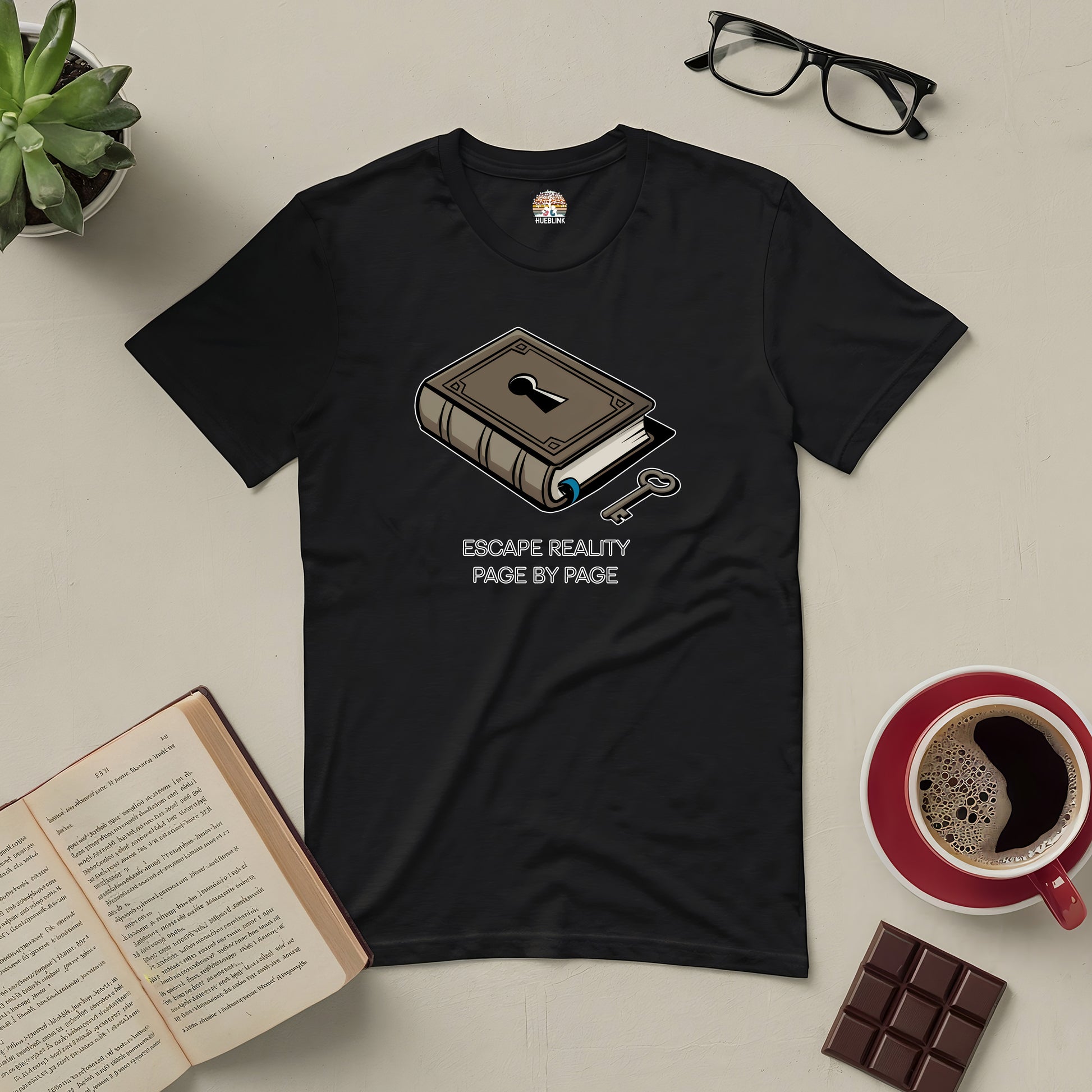 Black "Escape Reality Page by Page" tee with book design, surrounded by an open book, glasses, coffee, and chocolate bar.