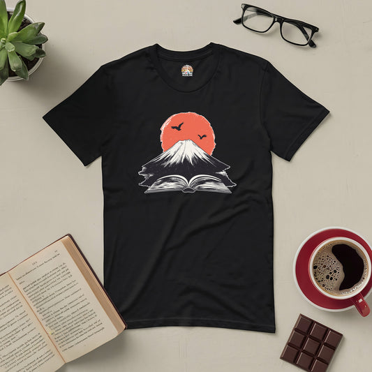 Black tee with a design of books forming a volcano, symbolizing the eruption of imagination, surrounded by coffee, chocolate, and reading glasses.