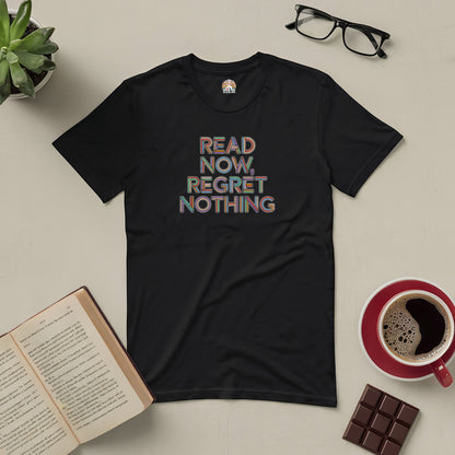 Black "Read Now, Regret Nothing" tee surrounded by a book, coffee, glasses, and chocolate on a beige table.