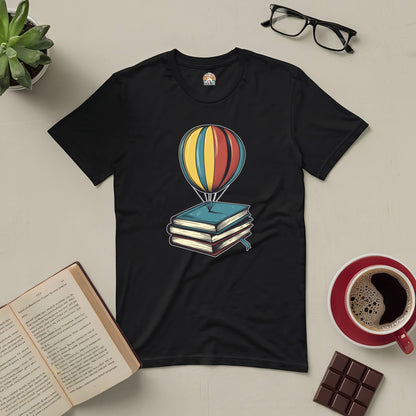 Whimsical Passport to Dreamland Tee with hot air balloon and books design, surrounded by coffee, glasses, chocolate, and plants.