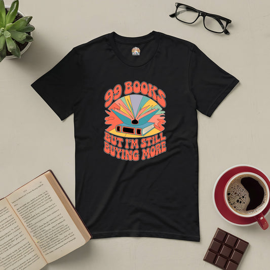 Black "99 Books and Counting!" tee showcasing book graphic, surrounded by open book, coffee, chocolate, glasses, and plant.