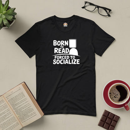 Black tee with "Born to Read, Forced to Socialize" text, next to an open book, glasses, coffee, and chocolate.