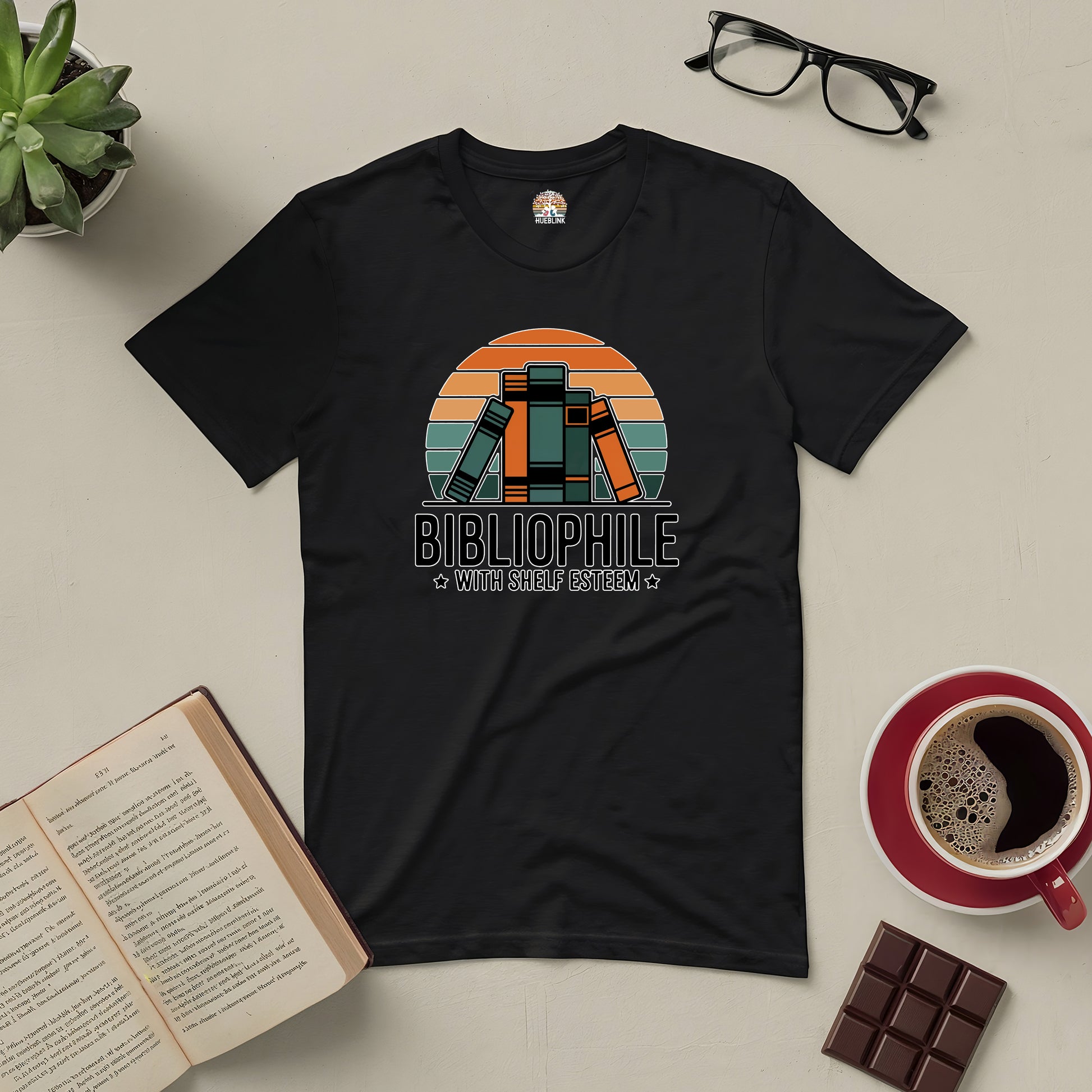 Retro-style "Bibliophile with Shelf Esteem" black tee featuring a book design, surrounded by book, coffee, and chocolate.