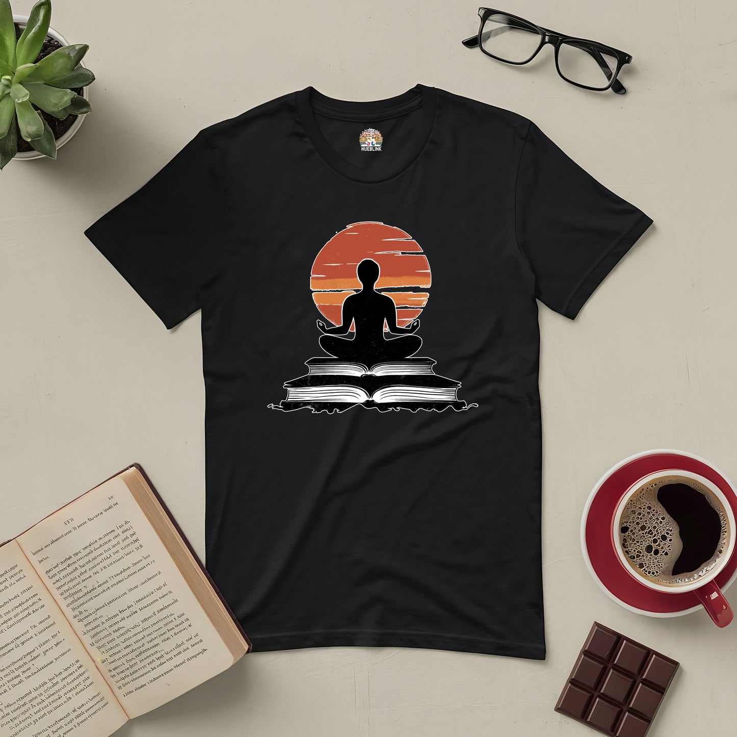 "Connection Established Tee with meditative reading design, surrounded by book, glasses, coffee, and chocolate on a table"