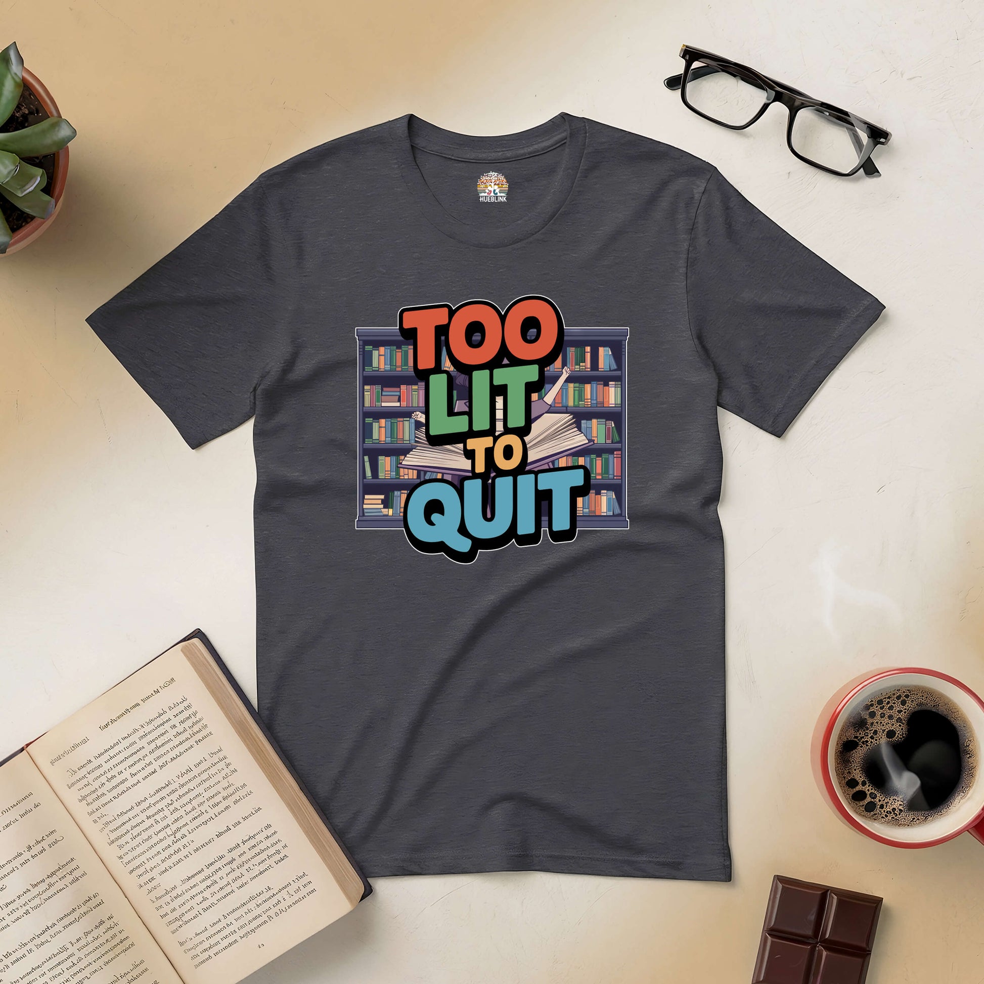 "Too Lit To Quit tee with book design, ideal for book lovers, displayed with a book, coffee, chocolate, and glasses"