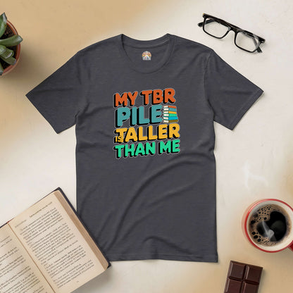 "Gray T-shirt with 'My TBR Pile is Taller Than Me' slogan, surrounded by books, coffee, and glasses, perfect for book lovers"