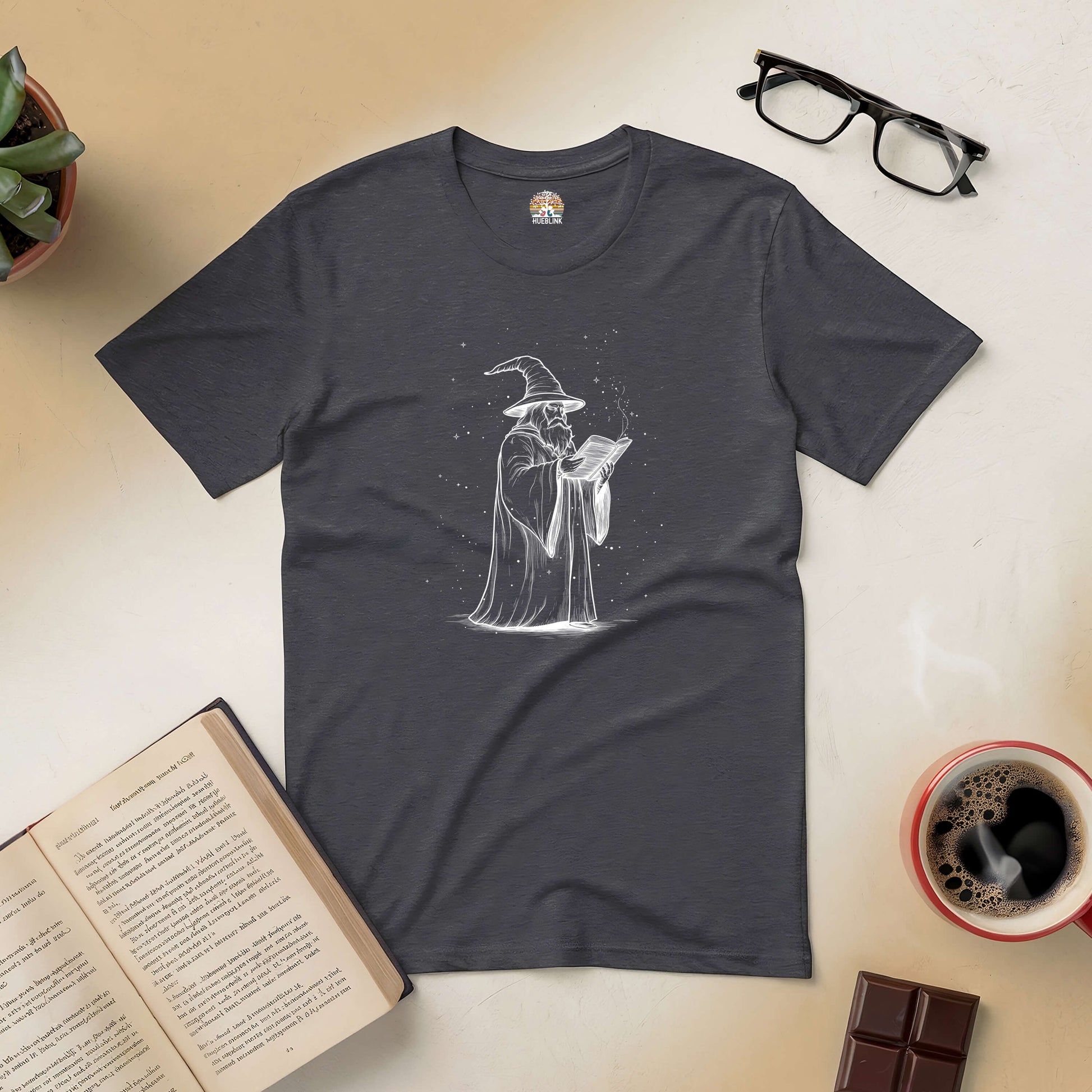 Wizard's Grimoire Tee with mystical design for fantasy lovers, featuring a wizard reading a book, surrounded by glasses, coffee, and chocolate.