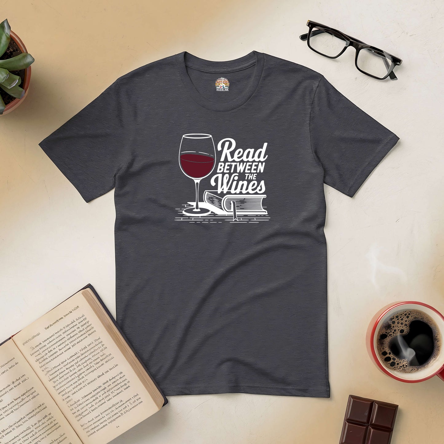 "Read Between the Wines tee with wine glass and book design, perfect for book and wine lovers, laid out with coffee and open book."