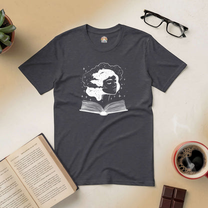 Universal Consciousness Tee featuring cosmic design with an open book, surrounded by coffee, chocolate, and reading glasses.