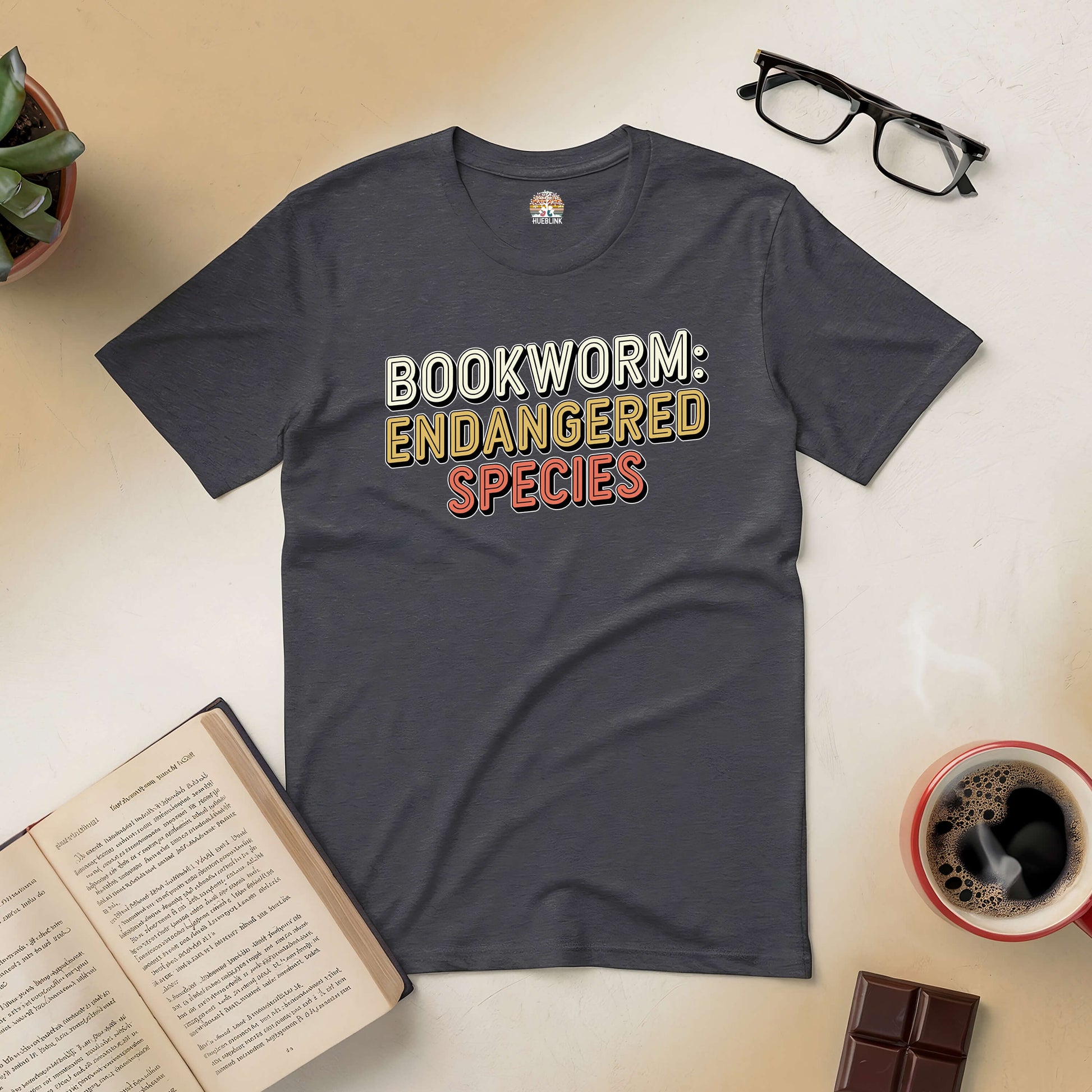 "Bookworm: Endangered Species Tee with books and coffee on a table, perfect for book lovers"