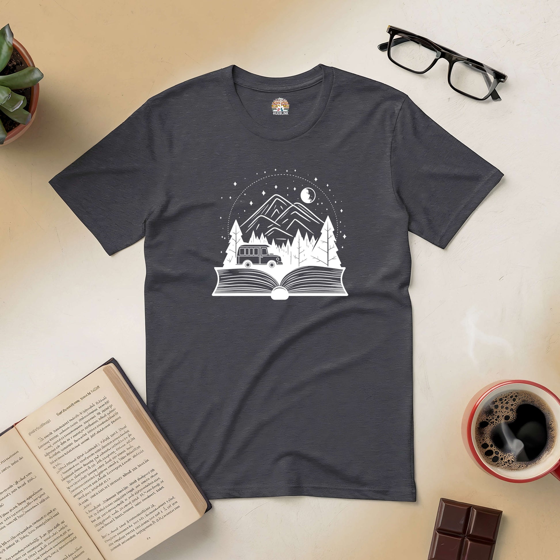 "A Trip From Cover To Cover Tee featuring a book-inspired design with a scenic adventure theme, shown with reading accessories"