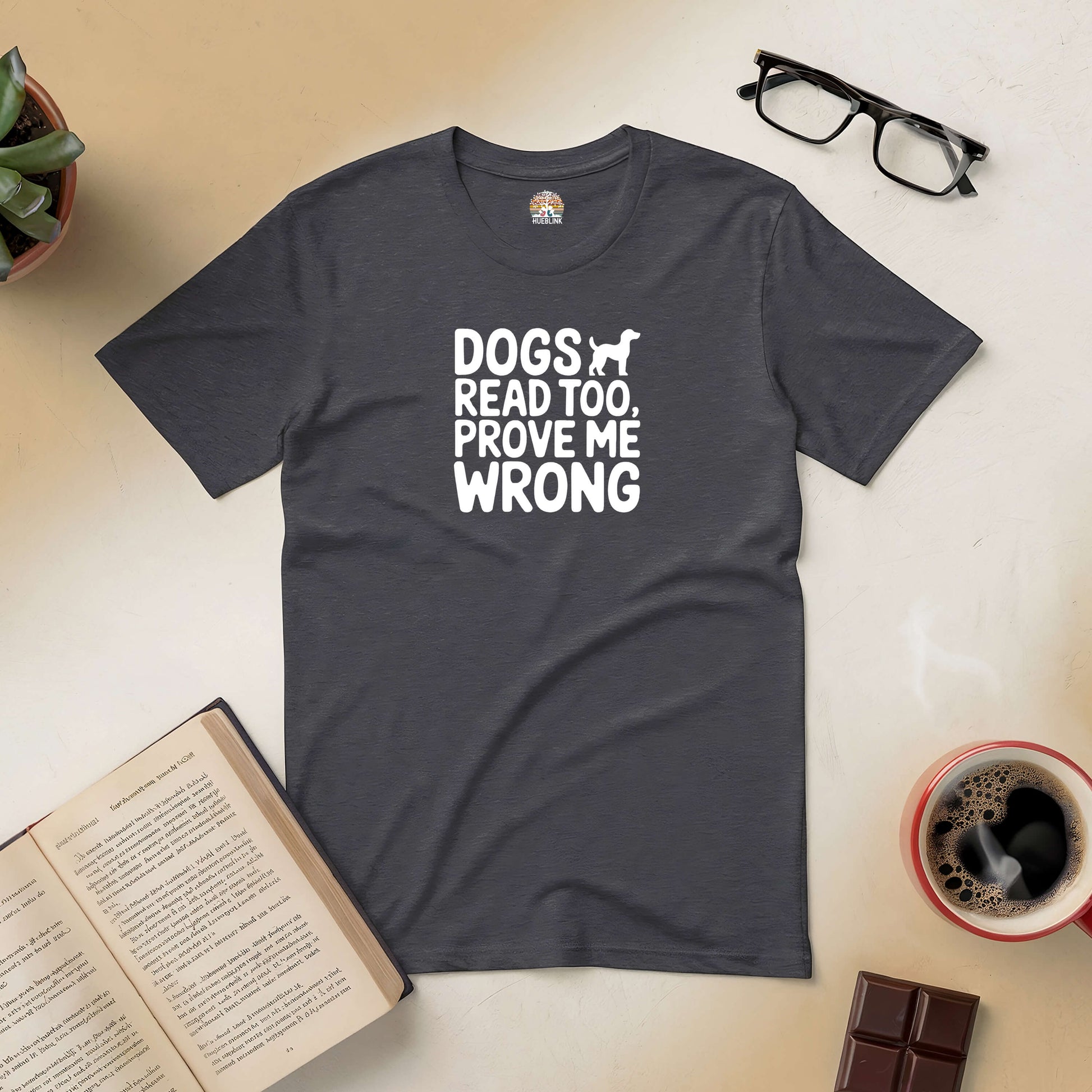 "Dogs Read Too, Prove Me Wrong" tee surrounded by a book, glasses, coffee, and chocolate bar.