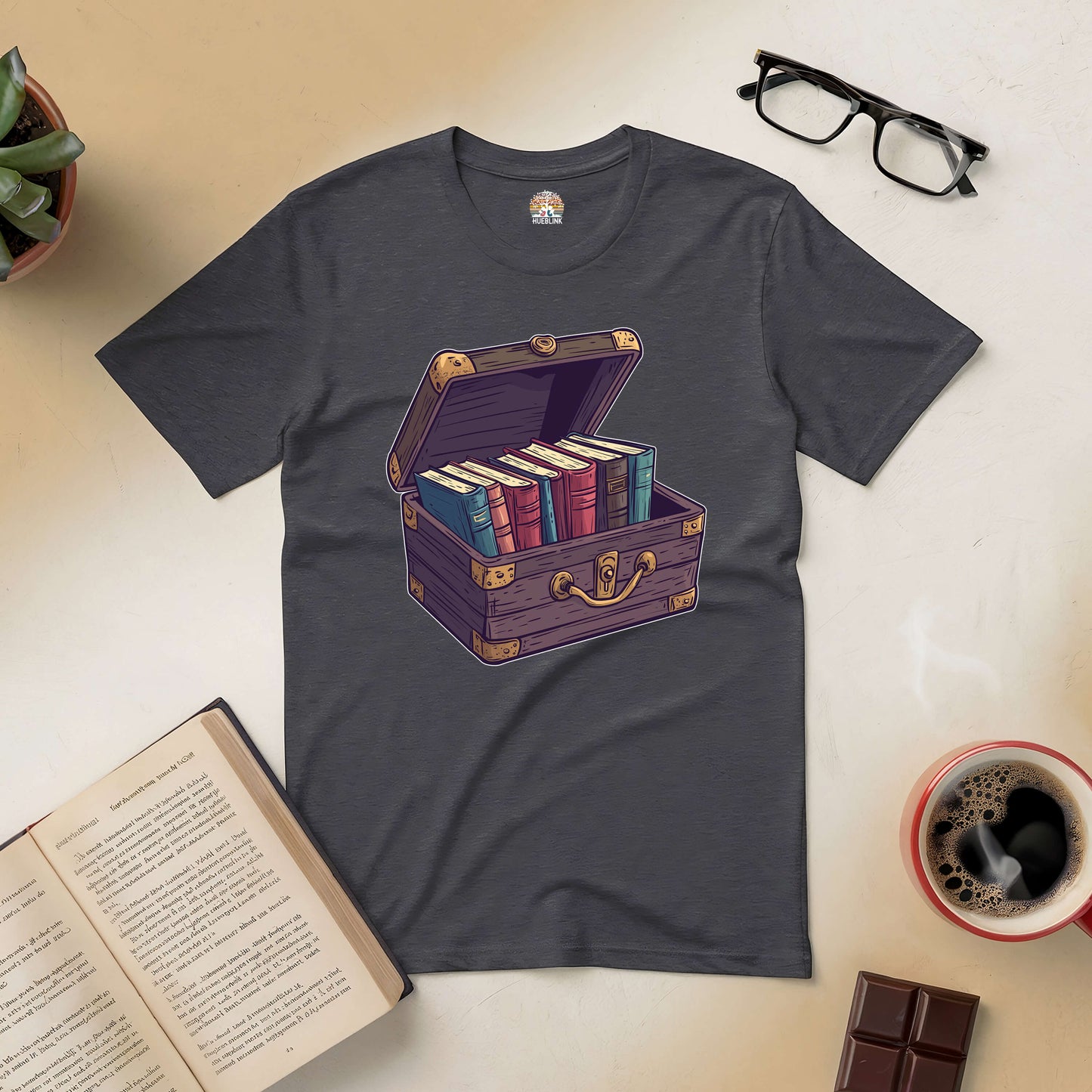 Dark tee with a treasure chest graphic filled with books, surrounded by coffee, glasses, and open novel, perfect for book lovers.