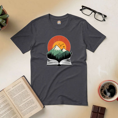 "Mountains of Imagination Tee with nature design over open book, surrounded by coffee, chocolate, and a plant."