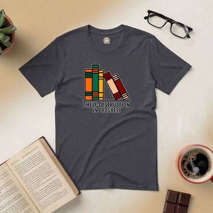 "Shelf-Destruction In Progress Tee with book graphics on a dark surface with open book, glasses, coffee, and chocolate nearby"