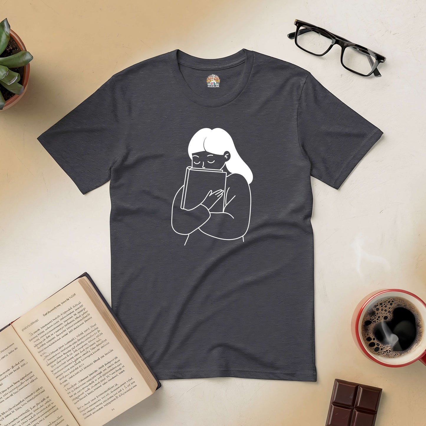 Black t-shirt featuring a minimalistic design of a girl hugging a book, surrounded by open book, glasses, coffee, and chocolate.