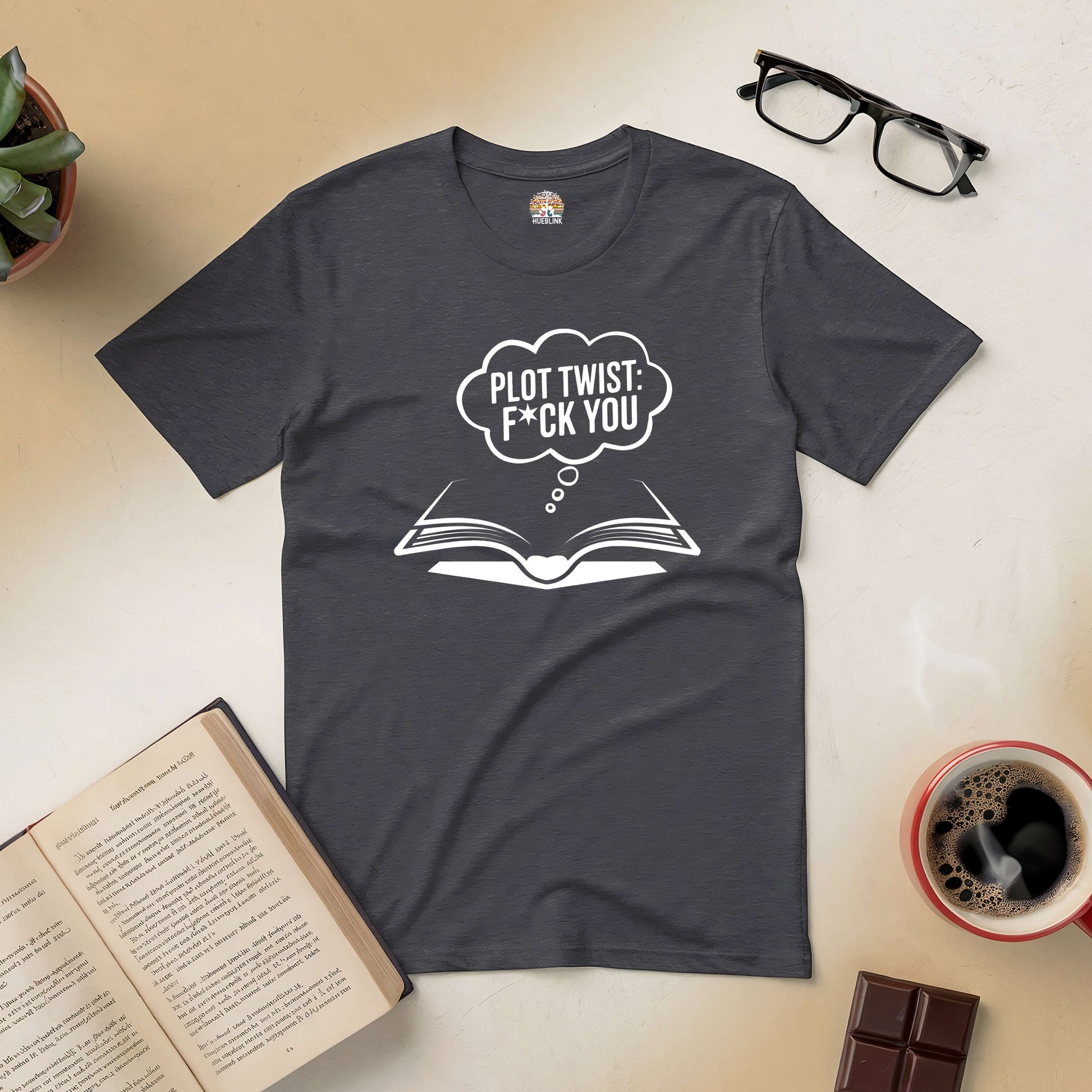 Black tee with "Plot Twist: F*ck You" text, surrounded by an open book, humor apparel for book lovers, on a wooden table.