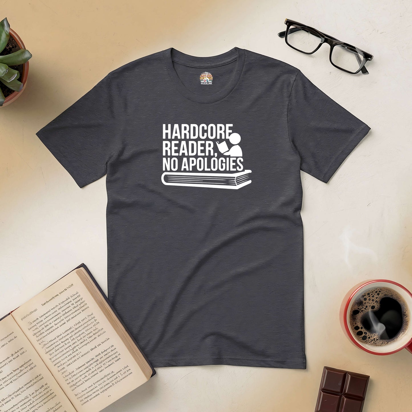 Charcoal tee with "Hardcore Reader, No Apologies" text, surrounded by books, glasses, coffee, and a chocolate bar.