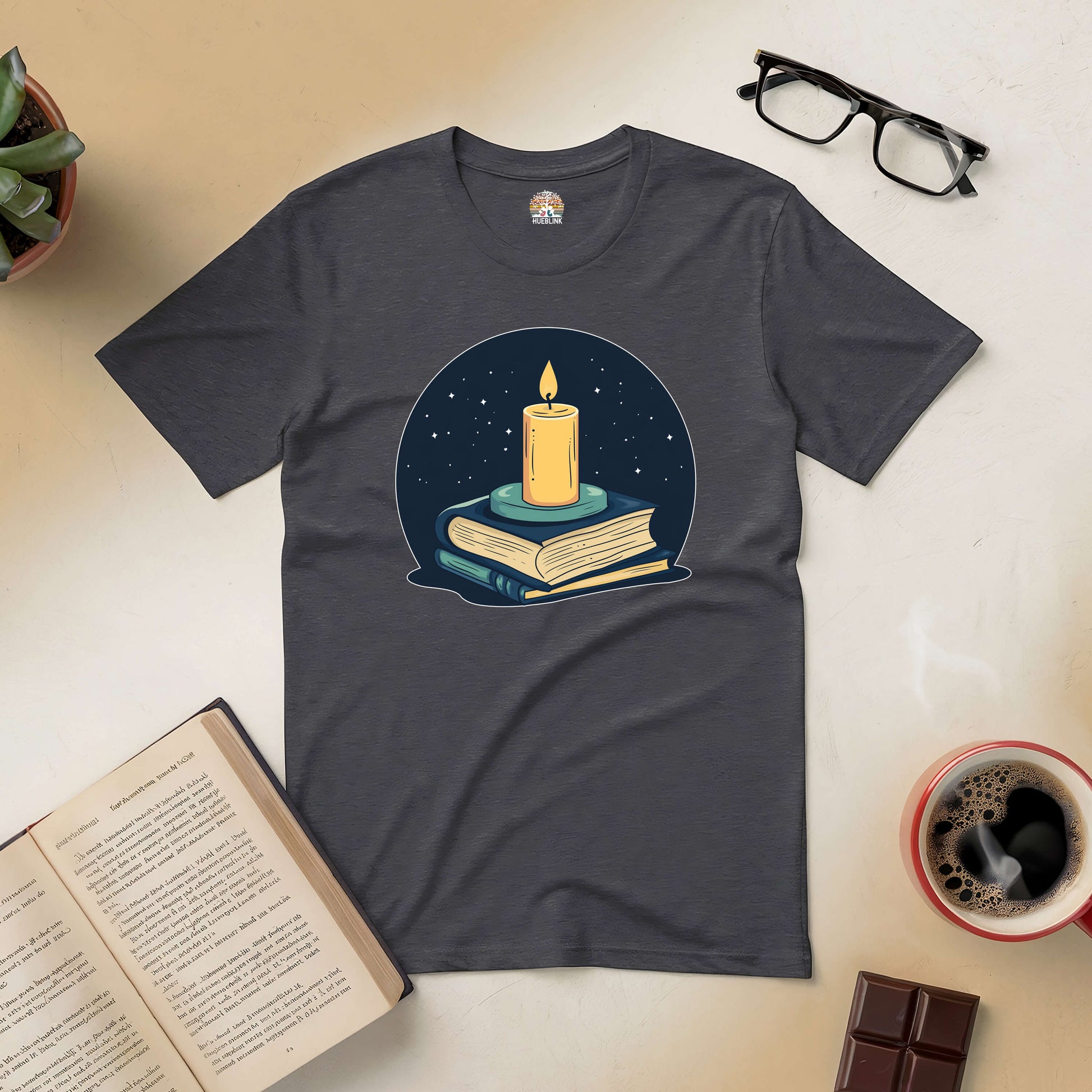 "Illuminate Your Mind Tee with candle and books design, surrounded by open book, coffee, and glasses for literary lovers"