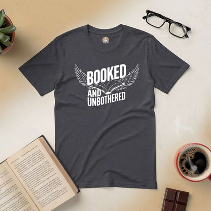 "Booked and Unbothered Tee with open book design, surrounded by coffee, glasses, and an open book on a cozy desk setup"