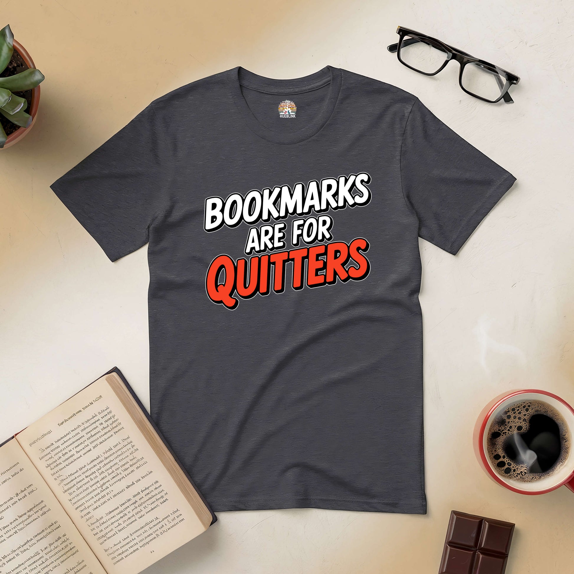 Charcoal tee with "Bookmarks Are for Quitters" text, surrounded by open books, coffee, and glasses on a table.