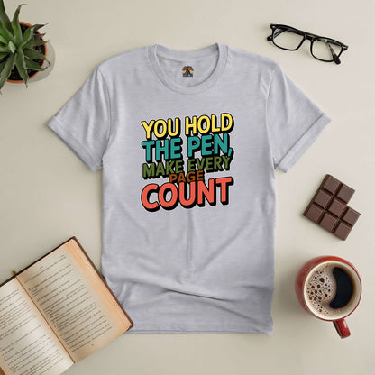 Inspirational tee with "You Hold the Pen, Make Every Page Count" design, perfect for living with purpose, surrounded by creative items.