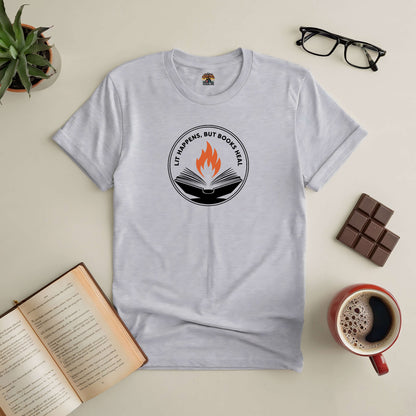 "Lit Happens, But Books Heal tee on table with open book, coffee, glasses, chocolate, and plant"