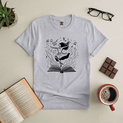 Dance Through the Pages Tee with book and whimsical design, surrounded by coffee, glasses, and a chocolate bar, celebrating storytelling.