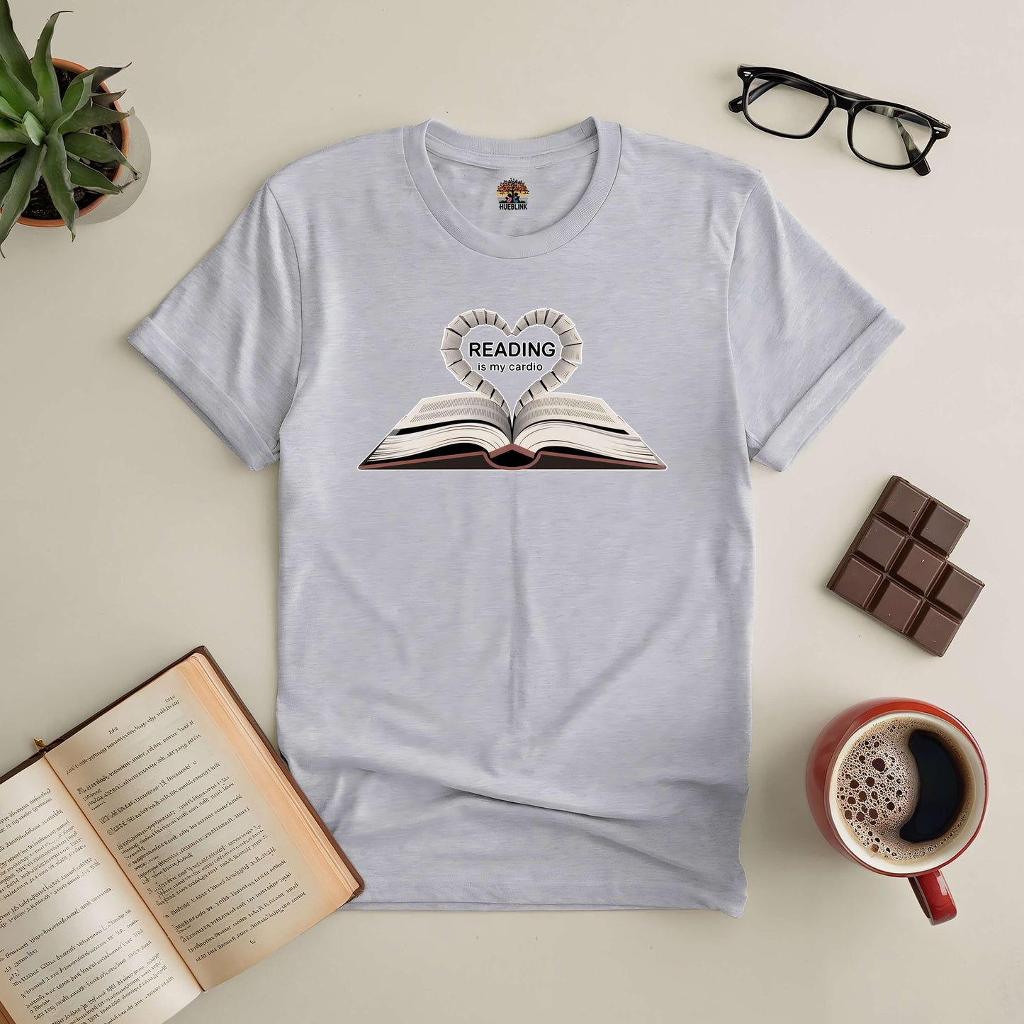 "Reading Is My Cardio tee displayed with open book, glasses, and coffee, perfect for book lovers"