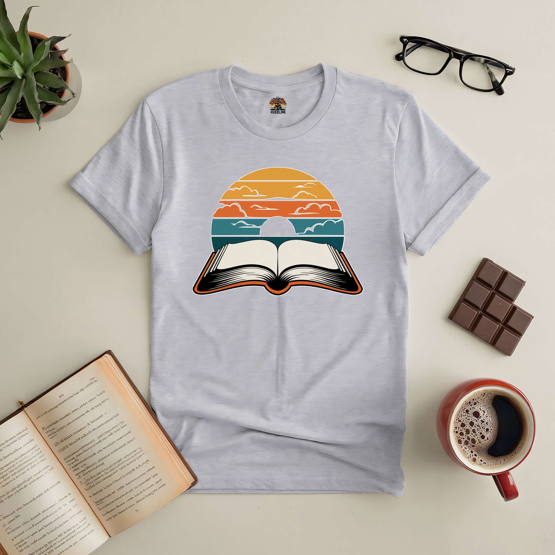 "Narratives in Color Tee featuring an open book under a vibrant dusk sky, symbolizing stories and colorful journeys in reading."