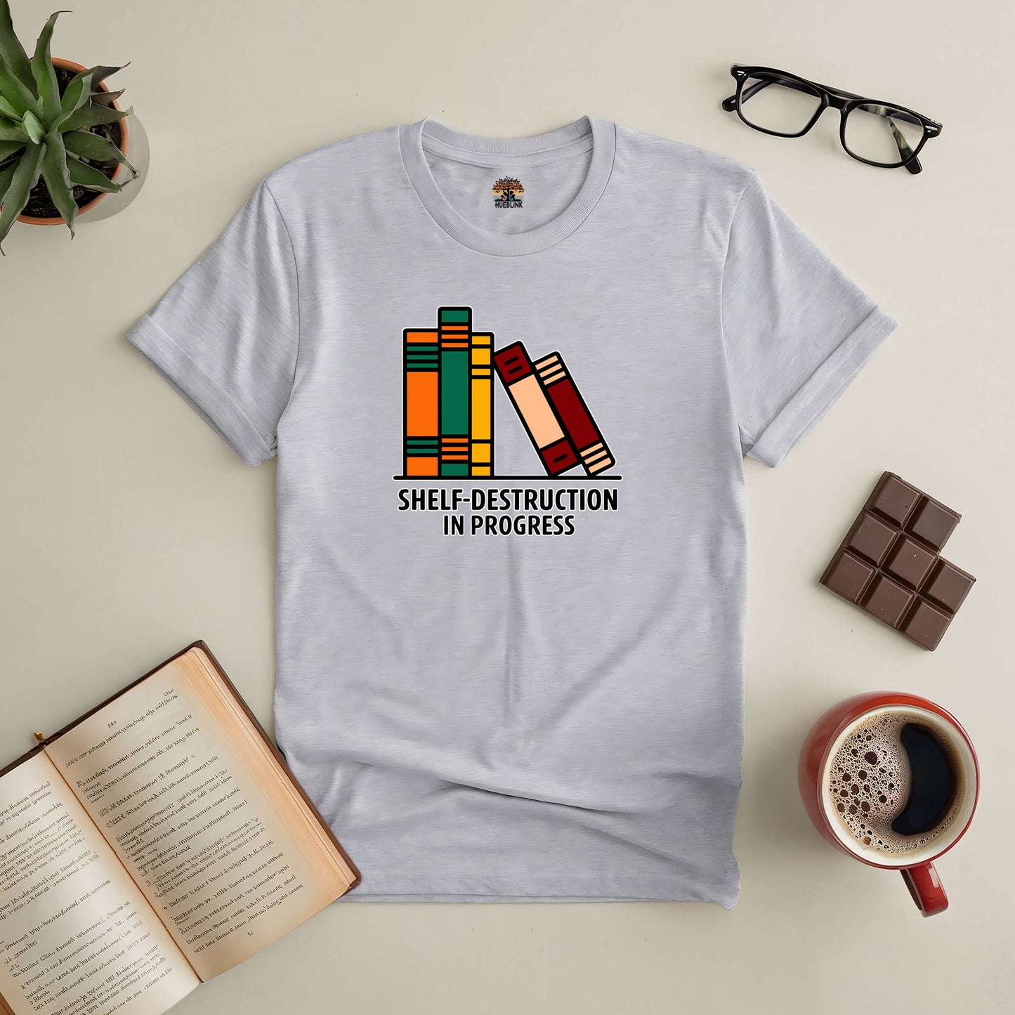 "Shelf-Destruction In Progress Tee with book graphic, perfect for book lovers, displayed with coffee, glasses, and chocolate."