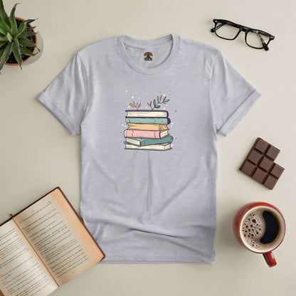 Blooming Books Tee with pastel-colored books and floral accents, surrounded by an open book, coffee, glasses, and chocolate.