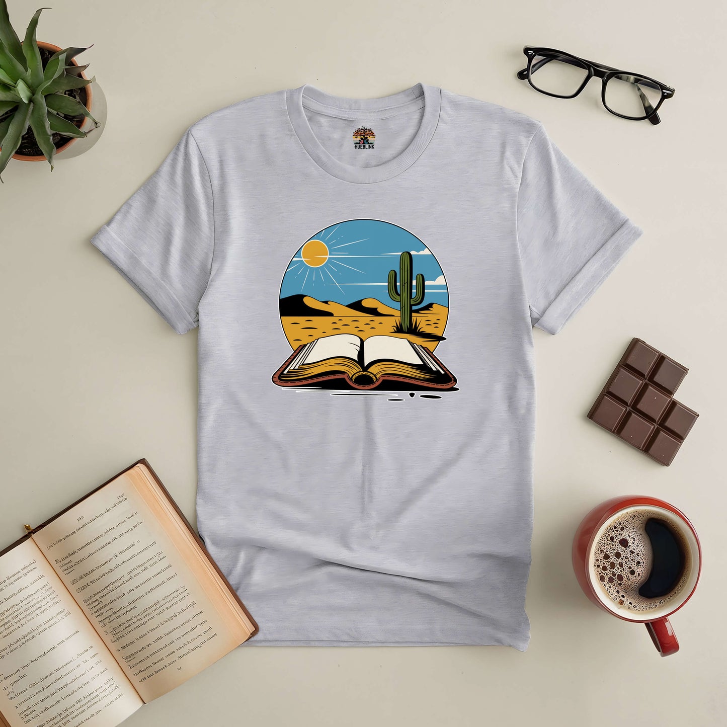 Silent Desert Tee featuring open book and cactus design, surrounded by coffee, chocolate, and reading accessories.