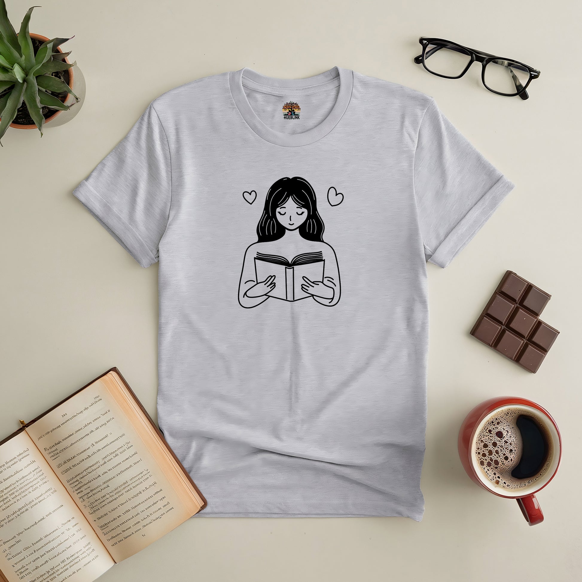 "Bookish Bliss Tee with reading design, perfect for book lovers, surrounded by coffee, chocolate, and open book"