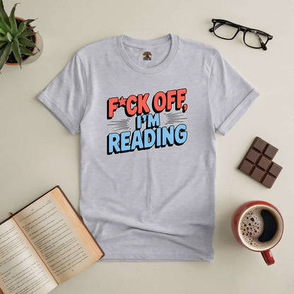 Light grey t-shirt with bold text "F*ck Off, I'm Reading," surrounded by a book, coffee, glasses, chocolate, and plant.