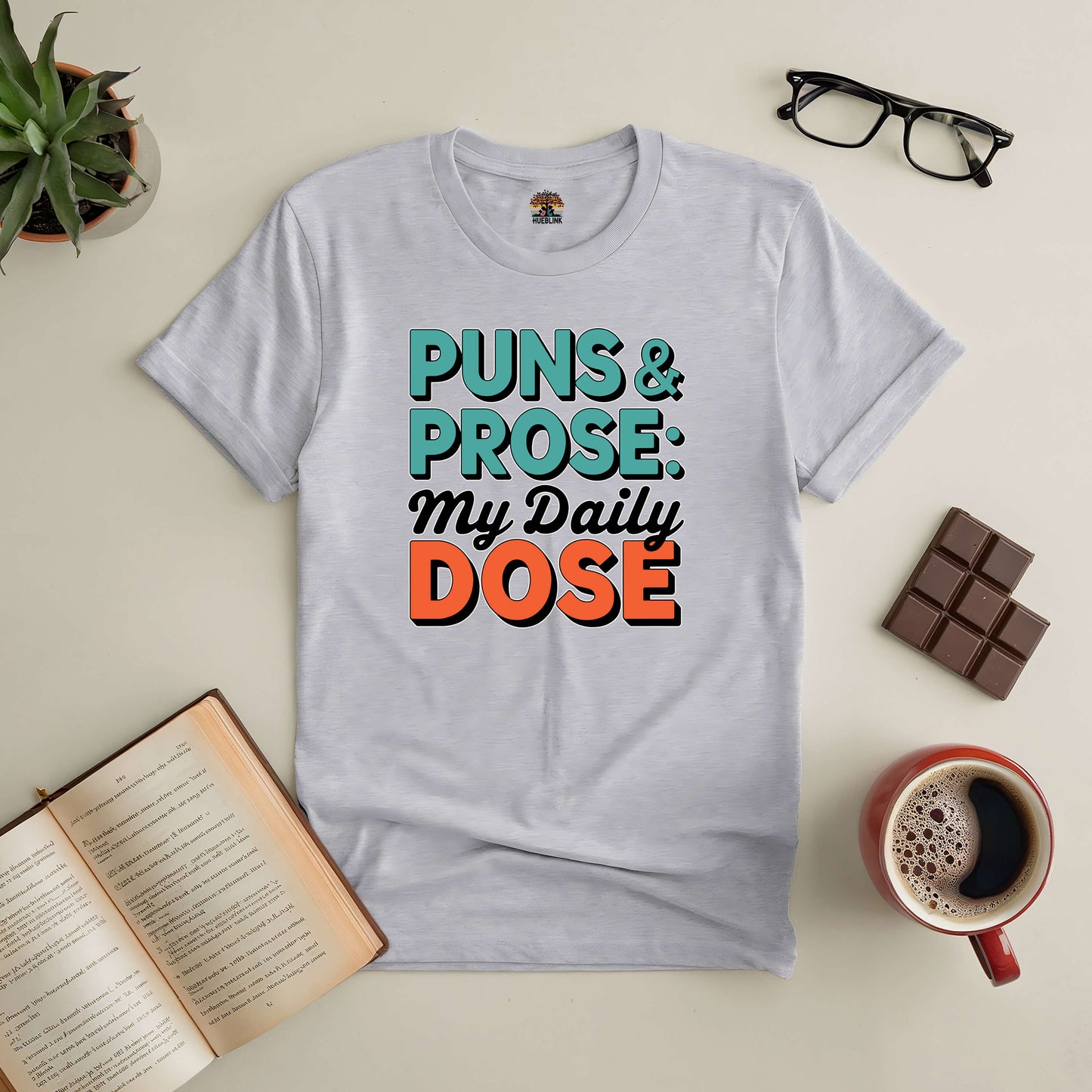 Puns & Prose: My Daily Dose Tee with witty wordplay design, surrounded by books, coffee, and chocolate for literary lovers.